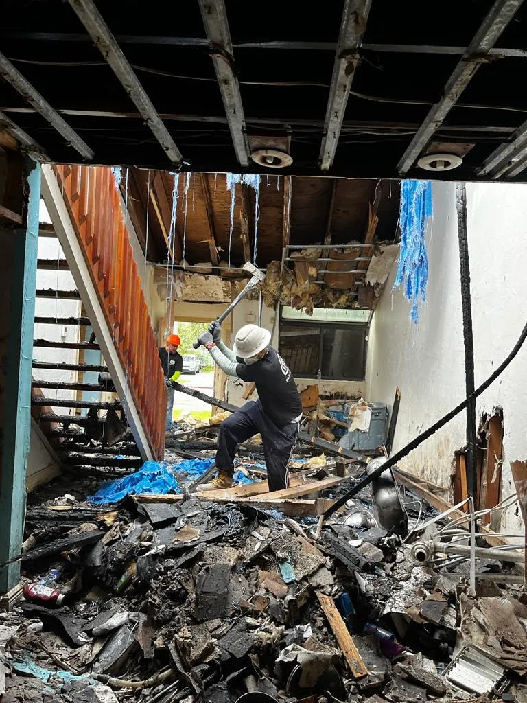 A crew member clears burned debris from a fire-damaged structure down to the framing.