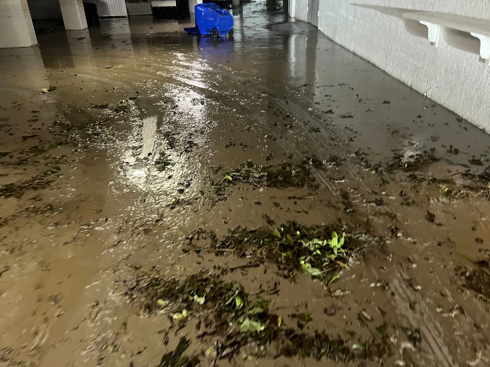 Mud and storm debris covering a flooded garage floor after heavy rain.